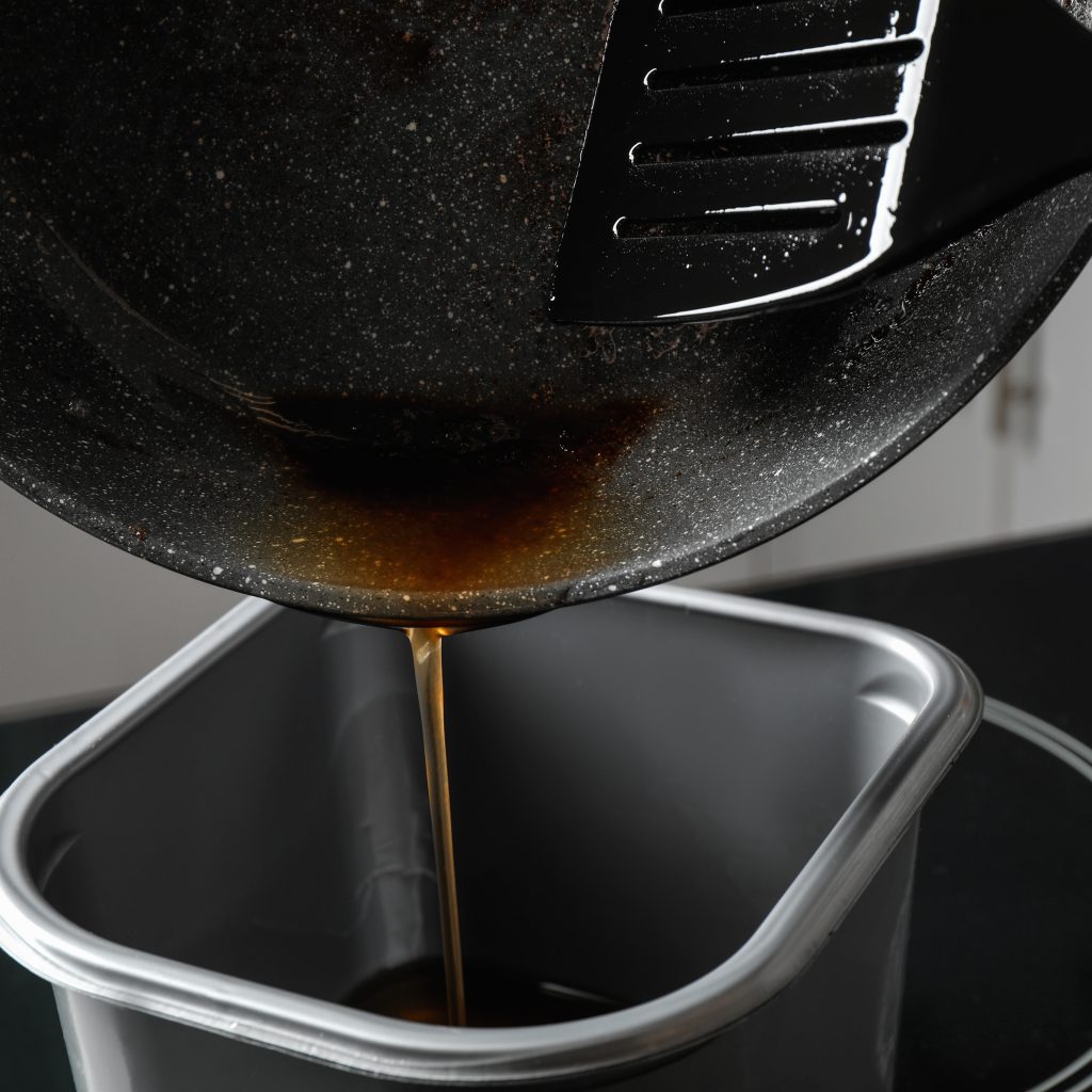 Pouring used cooking oil from frying pan into container, closeup